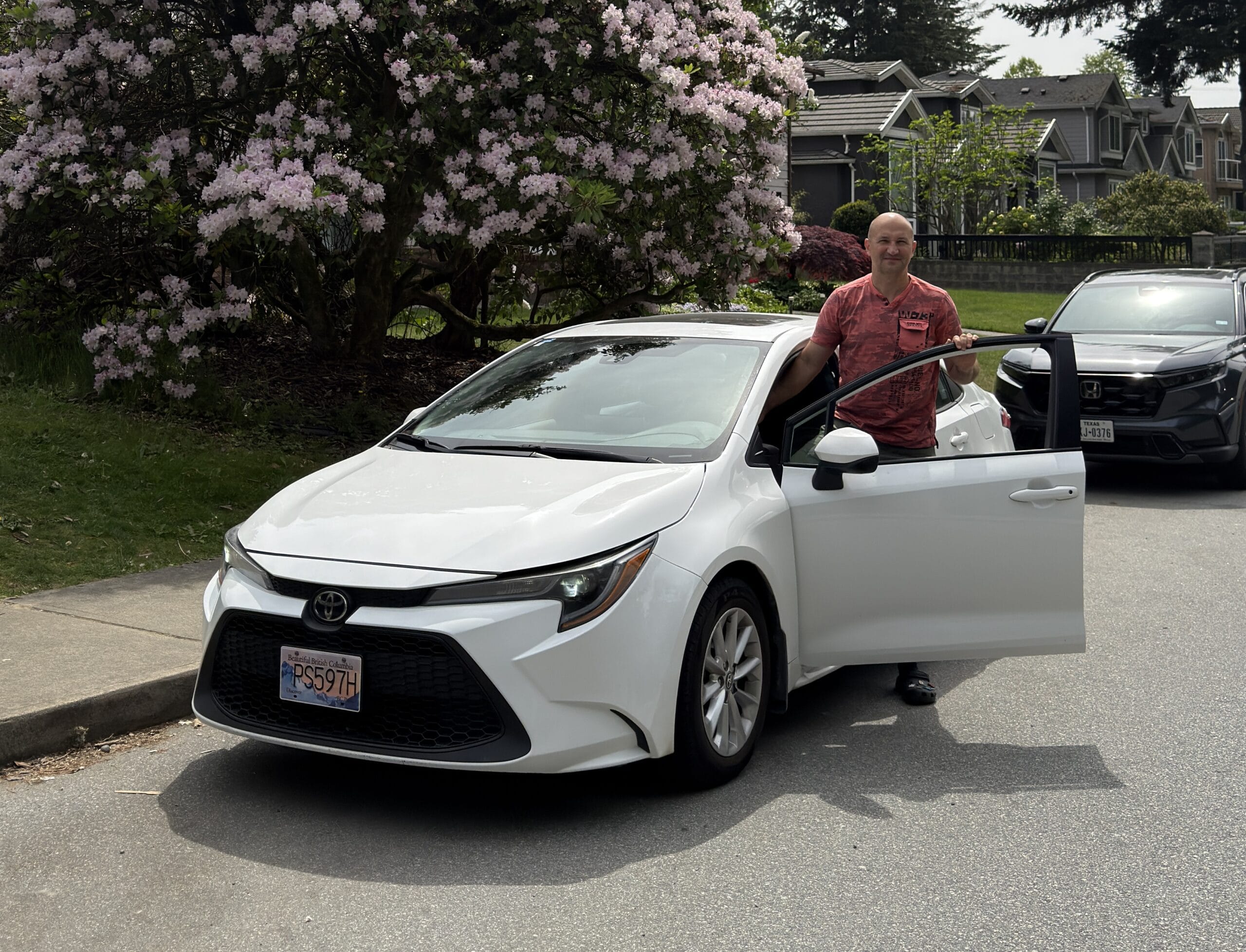 A man wearing red shirt entering a white toyota corolla sedan car