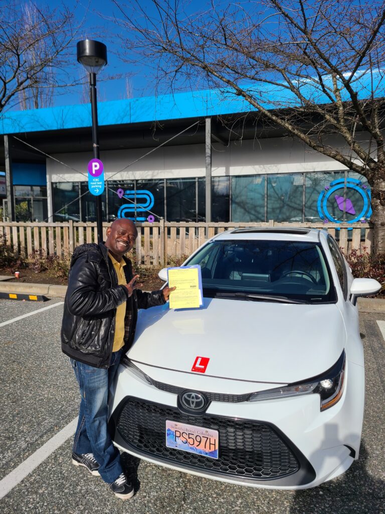 A man wearing a black hoodie with black joggers and white shoes holding papers standing beside white toyota corolla.